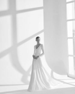 Préndate de Rima, un vestido de dos piezas formado por un traje y una capa de crepé fluida. Una boda eclesiástica en otoño es el marco ideal para lucir este modelo de línea A y escote de pico. Su sencilla manga larga compensa a la perfección la espalda descubierta y la cintura bordada. Tiendas de vestidos de Novia en Toledo, El Clavel