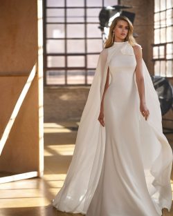 Vestidos de novia 2025 en Toledo. El Clavel. Vestido de novia de dos piezas, de corte sirena y estilo elegante, confeccionado en crepé. Presenta un escote halter, una espalda lágrima sin mangas y una capa de georgette con un lazo. Un delicado conjunto Aire Atelier.