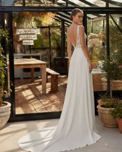 Modelo Ula - Vestido de novia largo de estilo sencillo y fluido, realizado en crepé combinado con encaje y pedrería. Presenta un escote halter, una espalda en V y un adorno cut out con encaje. Un look de tendencia Aire Boho. Tiendas de vestidos de Novia en Toledo, El Clavel